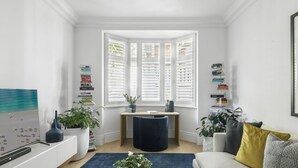 A bright, white room with a bay window, a desk with a chair, a bookshelf, and a sofa with cushions. - Uber Luxury 4 Bed Home with Pool in Mosman (Mosman)