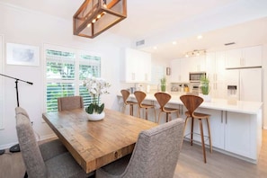 Una cocina moderna con armarios blancos, una mesa de comedor de madera y un amplio ventanal con persianas.