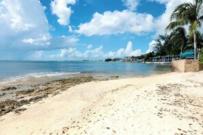Ein Strand mit blauem Himmel, sandigem Ufer und einigen Gebäuden im Hintergrund.
