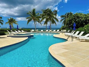 Une piscine entourée de chaises longues blanches et de palmiers.