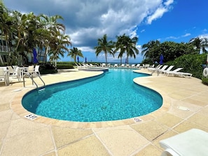 Una piscina con agua azul cristalina, rodeada de sillones de descanso y palmeras.