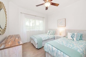 A bedroom with two beds, a ceiling fan, a large mirror, and a window with curtains. - Crescent Point Condo #9 - 3BR 7 Mile Beach Condo (George Town)