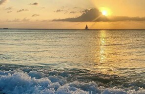 Un coucher de soleil sur une mer calme, avec un voilier à l'horizon.