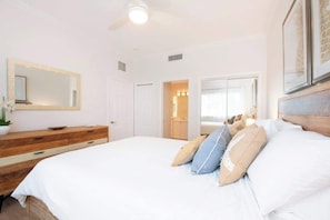 Un dormitorio con una cama, un aparador de madera, un espejo y una puerta que da a otra habitación.
