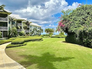 A well-maintained lawn, a building with balconies, and a hedge with pink flowers.