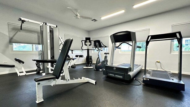 A gym with various exercise equipment, including a treadmill, elliptical, and weight machines. - Crescent Point Condo #9 - 3BR 7 Mile Beach Condo (George Town)