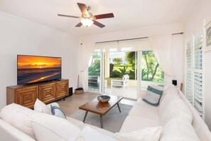 A living room with a flat-screen TV, a wooden cabinet, a white sofa, and a ceiling fan. - Crescent Point Condo #9 - 3BR 7 Mile Beach Condo (George Town)