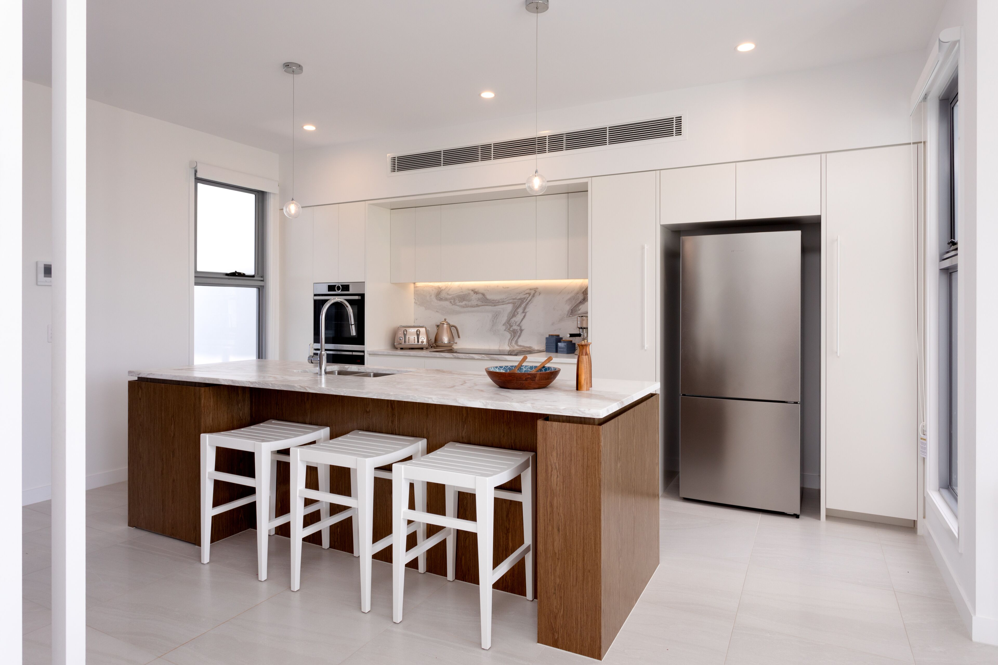 A modern kitchen with a marble countertop, stainless steel appliances, and white bar stools.