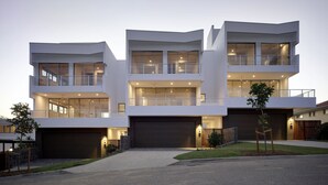 A modern multi-story house with a garage, large windows, and a well-lit entrance. - The Beach Houses Holiday Villas (Coolangatta)
