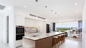 A modern kitchen with a large island, built-in appliances, and a view of the city. - The Beach Houses Holiday Villas (Coolangatta)