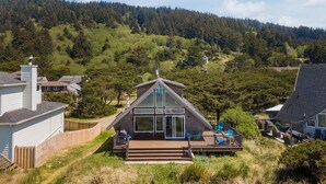 A house with a large glass front, a deck, and a view of a forested hill. - The Lookout - Beachfront, amazing views, spacious home (Cloverdale)