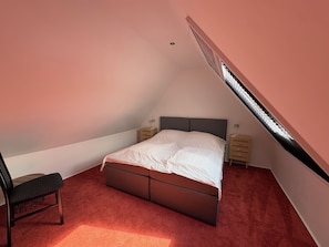 A bedroom with a sloped ceiling, a bed, a chair, and two bedside tables.