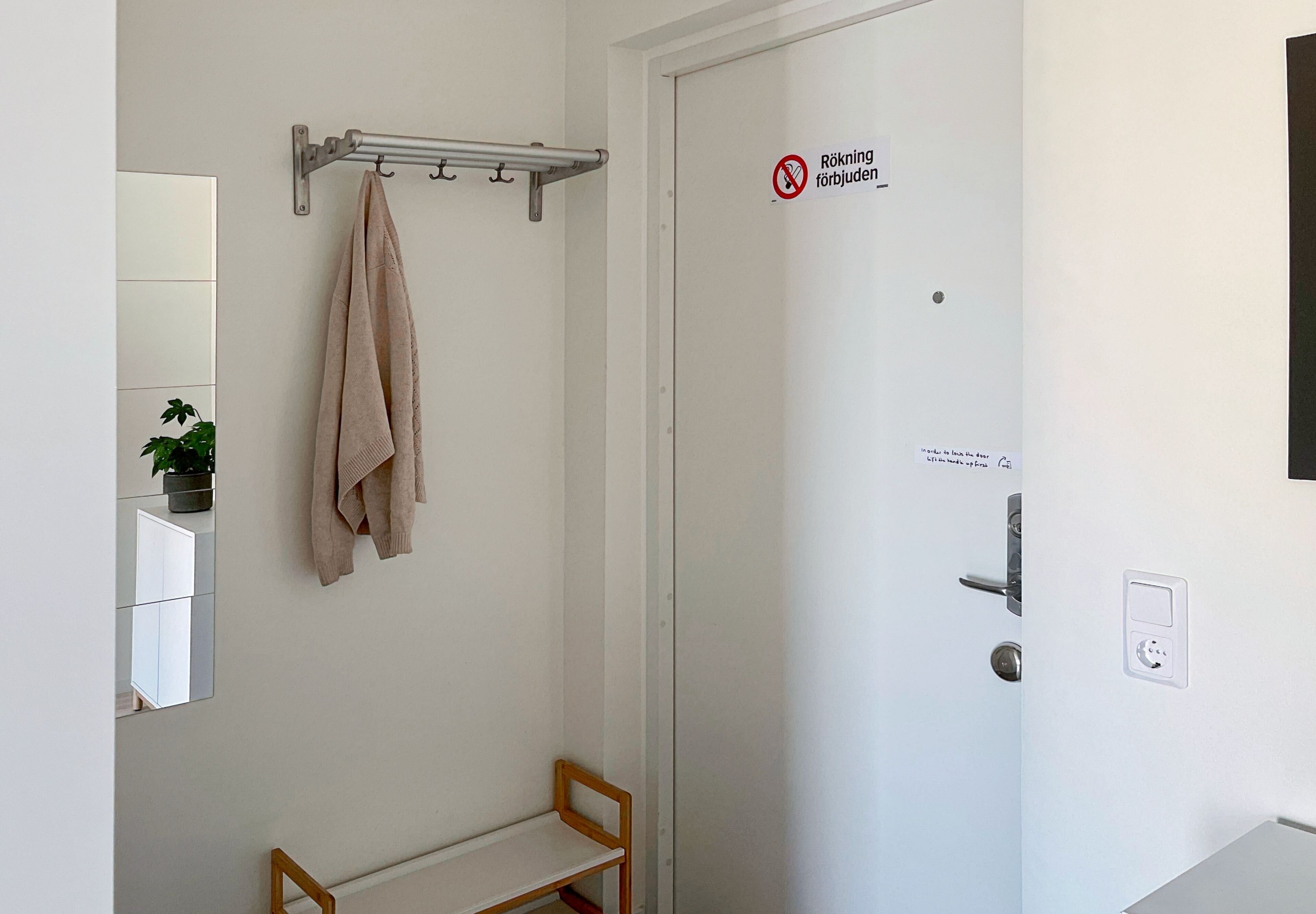 Une salle de bain équipée d’un porte-serviettes, d’un banc, d’une porte avec une pancarte et d’un miroir.
