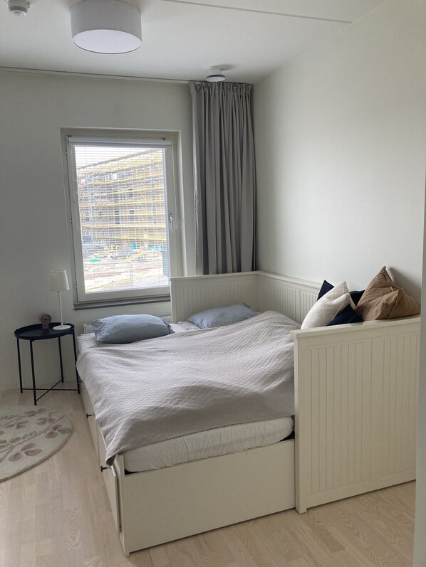 Une chambre à coucher avec un lit, une fenêtre avec des rideaux, une petite table et un radiateur.