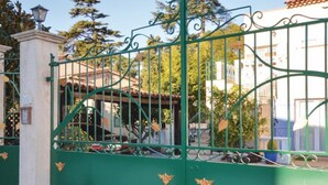 A gated entrance with a wrought iron gate, a stone pillar, and a building with a tiled roof in the background. - Villa with terrace 300 m from the sea (Antibes)