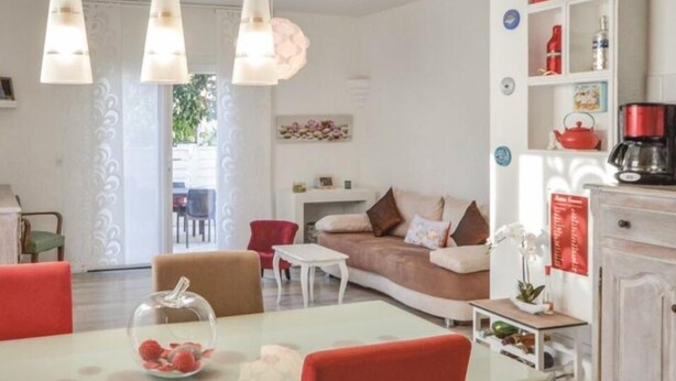 A living room with a sofa, red chairs, a coffee table, and a dining table. There are pendant lights, a cabinet, and a shelf with items. - Villa with terrace 300 m from the sea (Antibes)