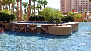 A pool area with a hot tub, palm trees, and a building in the background.