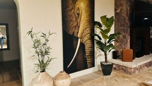A hallway with a large elephant painting, two potted plants, and a stone fireplace.