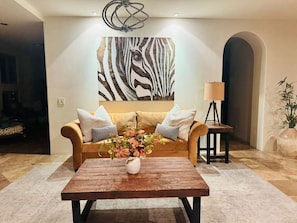 A living room with a sofa, a coffee table with flowers, a zebra print wall art, a lamp, and a plant.