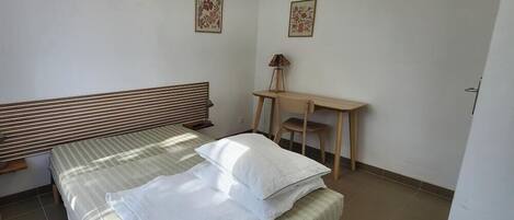 A bedroom with a bed, a desk, and two framed pictures on the wall.