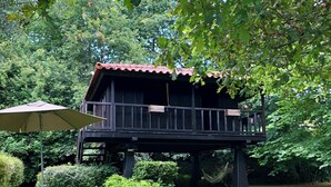 A wooden cabin with a balcony, surrounded by lush greenery and a well-maintained lawn.