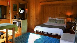 A wooden cabin with a bed, a small kitchenette, and a dining area.