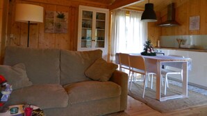 A cozy cabin interior with a sofa, dining table, chairs, and a kitchen area. - Treehouse Quinta Lamosa (Arcos de Valdevez)
