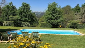 A rectangular swimming pool with a clear blue water surface, surrounded by a well-maintained lawn and bordered by green hedges. There are three wooden lounge chairs with green and white stripes positioned at the pool's edge. - Treehouse Quinta Lamosa (Arcos de Valdevez)