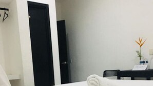 A hotel room with a neatly made bed, a black door, a small desk with a chair, and a plant on the desk. - Private room with king size bed num023 (Brisas de Zicatela)
