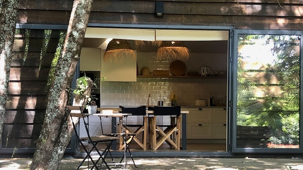 Een houten terras met een hangmat, een eettafel met stoelen en een keuken met een groot raam.