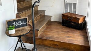 Una escalera de madera con barandilla de metal, un cartel que dice 'Hello', un reloj y maletas antiguas.