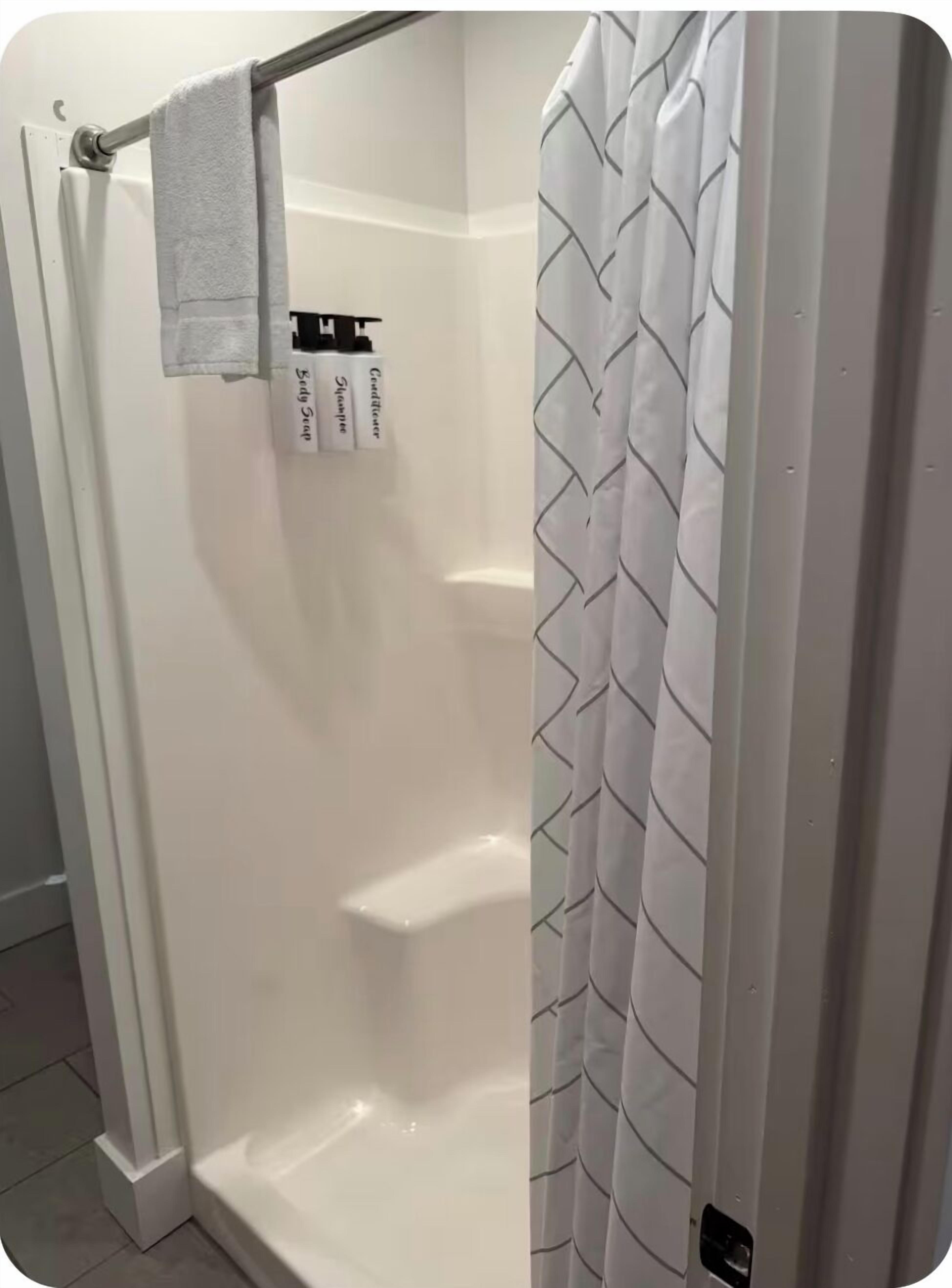 A shower with a white curtain and a towel hanging on a metal rod.