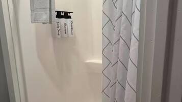 A shower with a white curtain and a towel hanging on a metal rod.