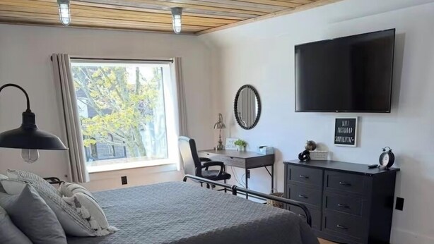 Un dormitorio con cama, escritorio, silla, cómoda, televisor y ventana con vistas.