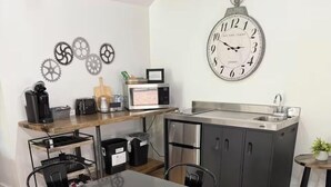 Cocina compacta con comedor, que incluye un reloj de pared, microondas y pileta.