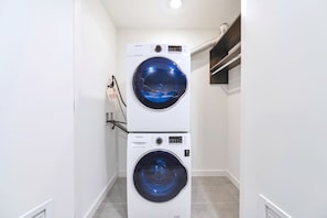 A laundry room with two stacked washing machines, a tiled floor, and a white wall. - Downtown Studio | Rooftop Pool | Walk to Bayside (Miami)