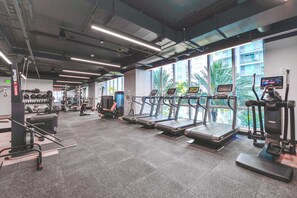 Ein Fitnessstudio mit Laufbändern, Krafttrainingsgeräten und einem großen Fenster mit Blick auf Palmen.