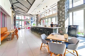Un restaurant moderne doté d’un bar, de différents espaces pour s’asseoir et offrant une vue sur la rue.
