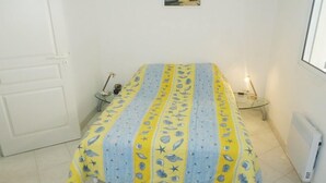 Een kleine, schone kamer met een bed, nachtkastje, lamp en een foto aan de wand.