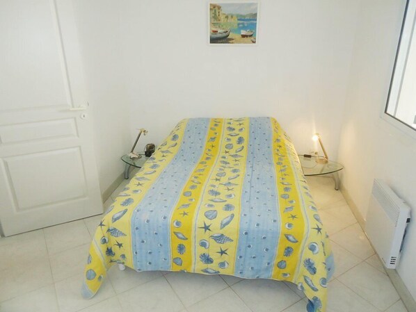 Una habitación pequeña y limpia con una cama, una mesita de noche, una lámpara y un cuadro en la pared.
