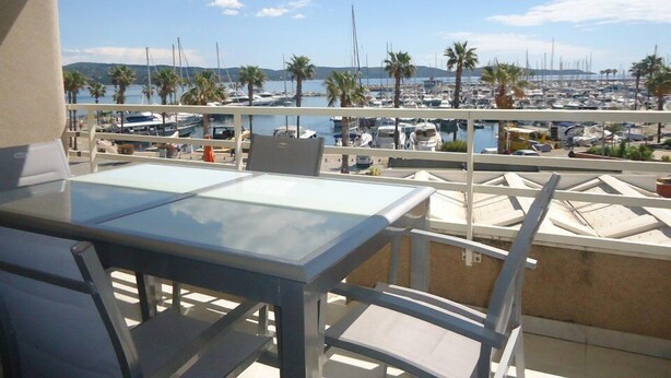 Een balkon met een tafel en stoelen met uitzicht op een jachthaven met boten en palmbomen.