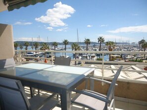 Un balcón con mesa y sillas que da a un puerto deportivo con barcos y palmeras.