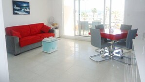 Een moderne woonkamer met een rode bank, een glazen salontafel, en een eethoek met een rode tafel en grijze stoelen.