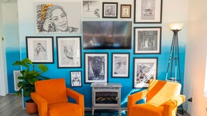 A room with two orange armchairs, a large TV, and various framed artworks on the wall. - Charming & Artsy Half-House, Walk to Best of Sedona! Views, Yard & Firepit (Sedona)