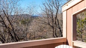 A wooden deck with a white Adirondack chair, a wooden railing, and a view of leafless trees and distant hills. - Charming & Artsy Half-House, Walk to Best of Sedona! Views, Yard & Firepit (Sedona)
