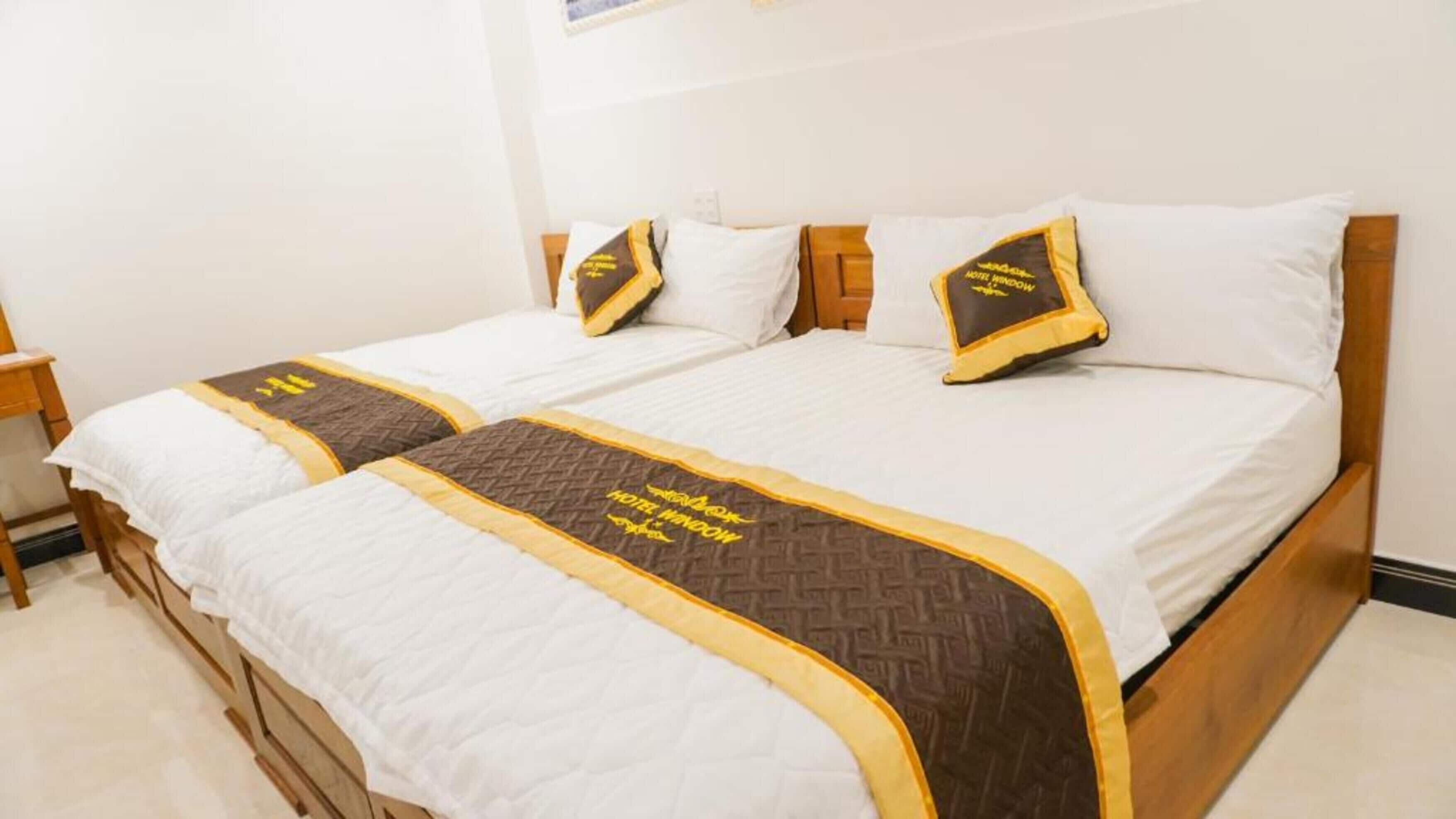 A double bed with white bedding and two decorative pillows, each with a gold and black design.