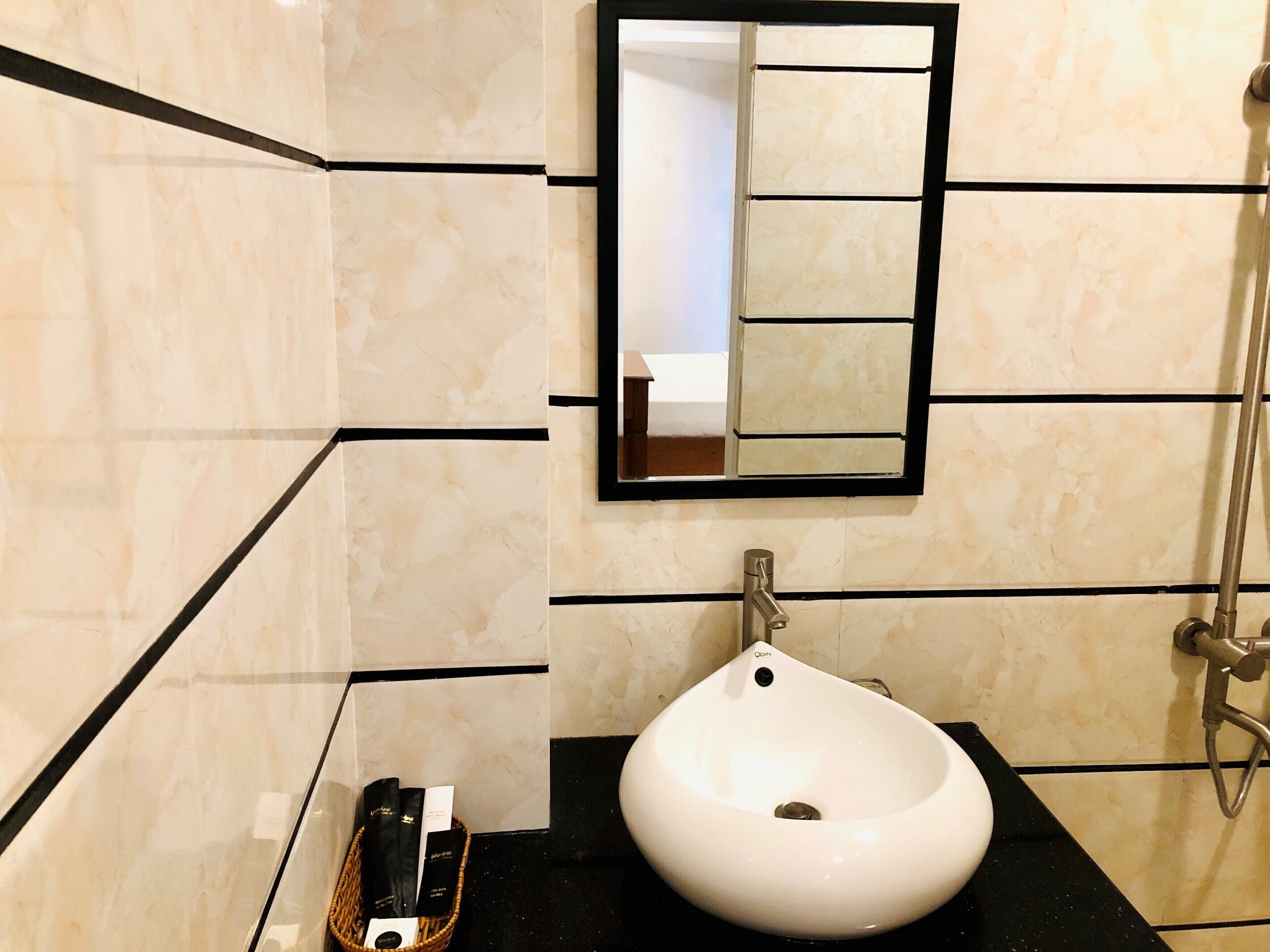Une salle de bain avec un lavabo blanc, un miroir et des murs recouverts de carreaux noirs.