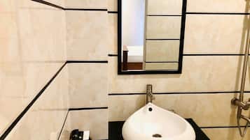 Une salle de bain avec un lavabo blanc, un miroir et des murs recouverts de carreaux noirs.