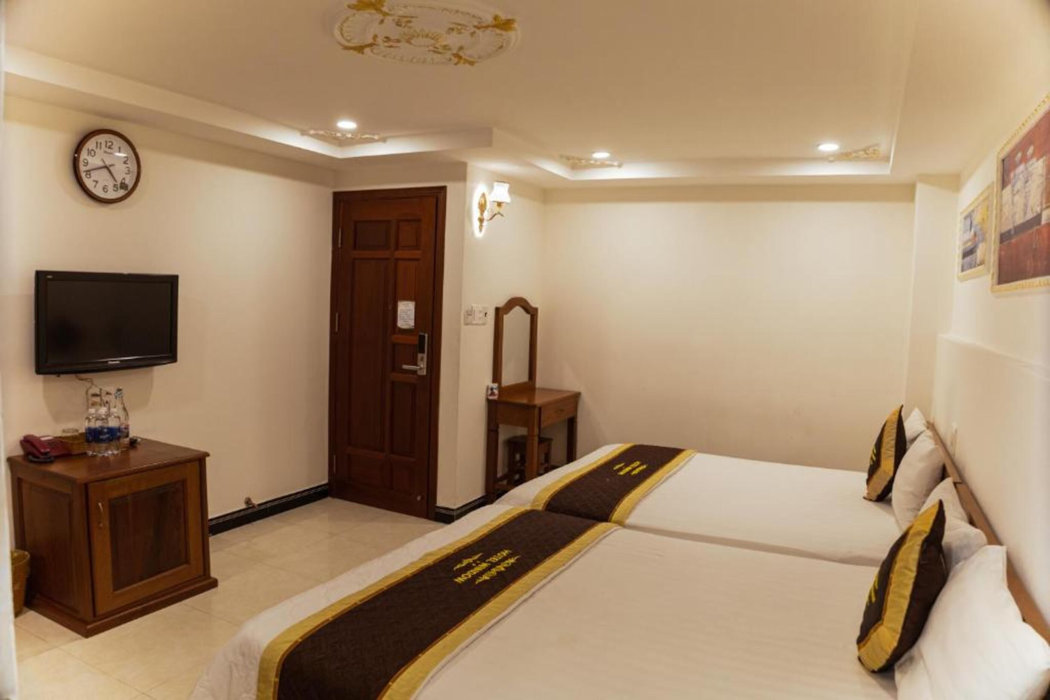 A hotel room with two beds, a television, a wooden cabinet, a clock, and a door.