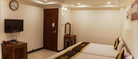 A hotel room with two beds, a television, a wooden cabinet, a clock, and a door.
